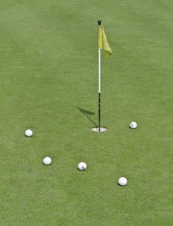 Five striped practice golf balls near hole with short flag on practice green